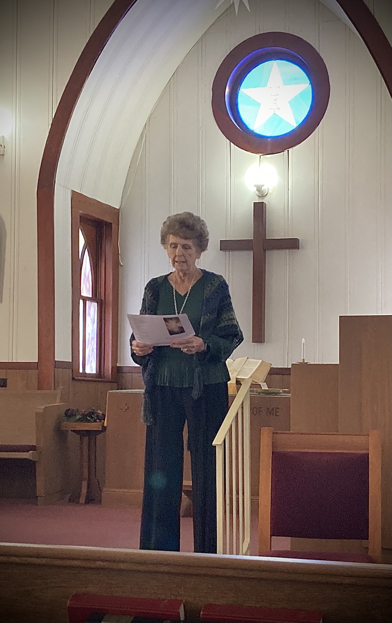 Pastor Judy Gotcher in the sanctuary, reading from a paper beneath the Texas star window.